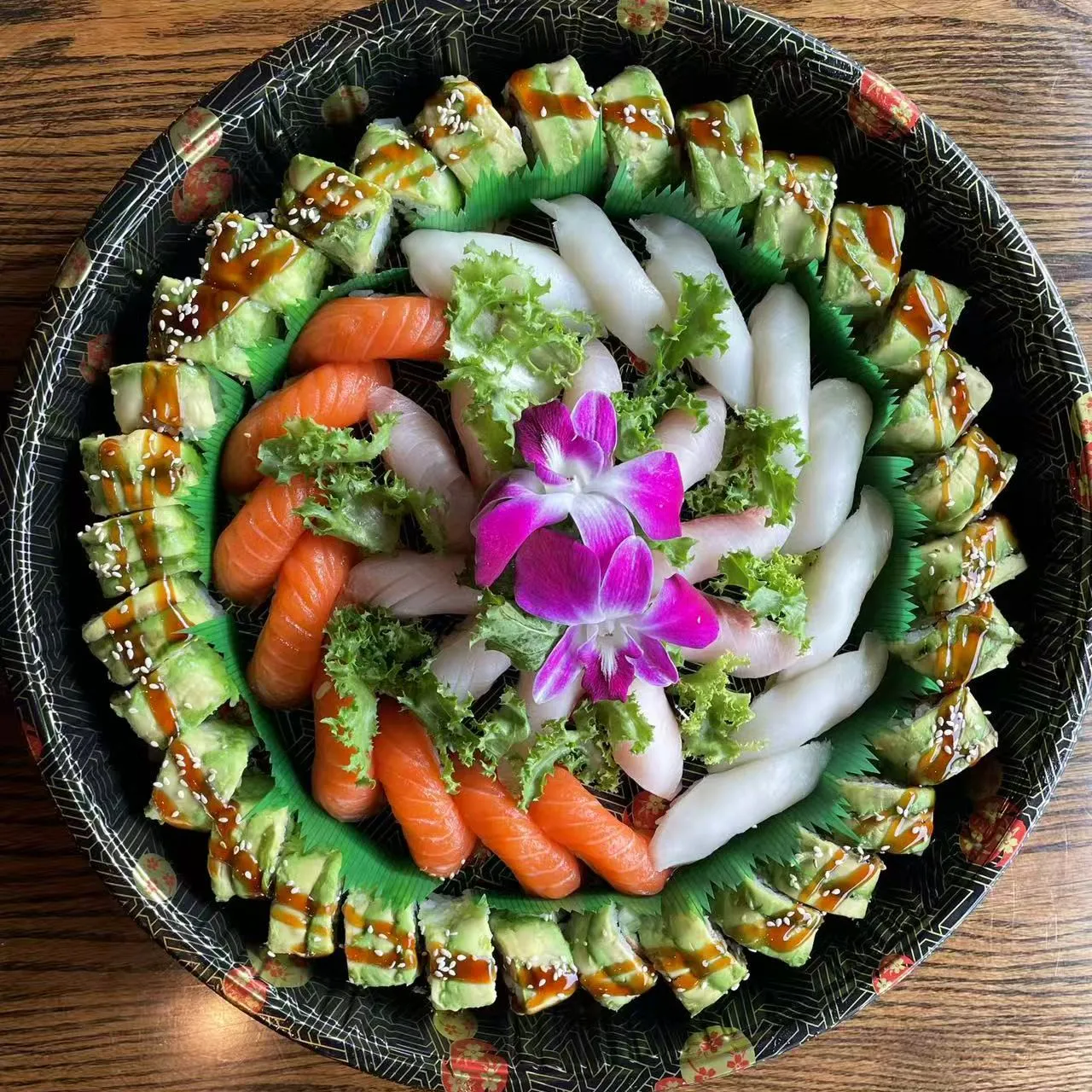 Round sushi platter with assorted nigiri, sushi rolls and purple orchid garnish
