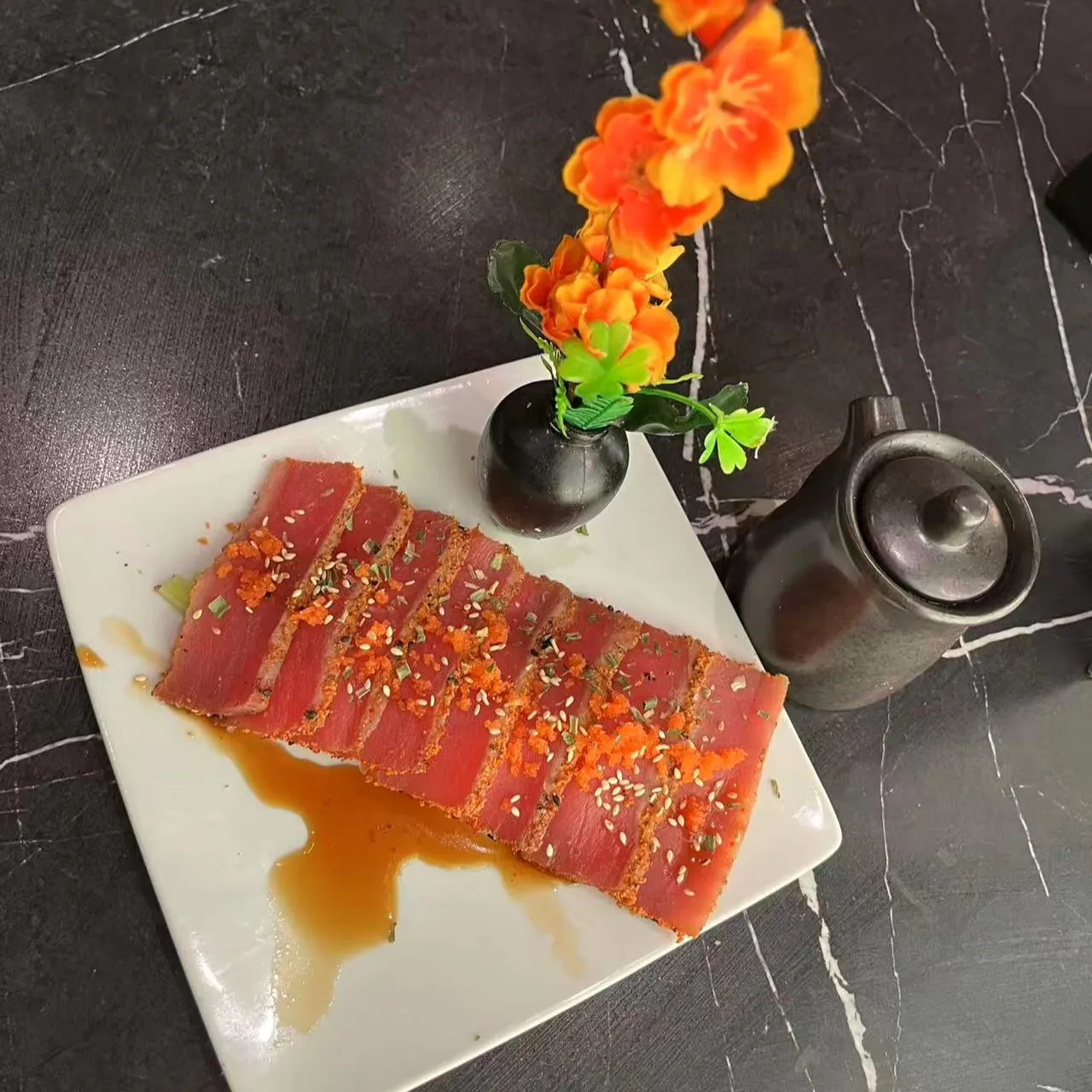 Seared tuna sashimi slices with sauce, tobiko and sesame garnish on white plate