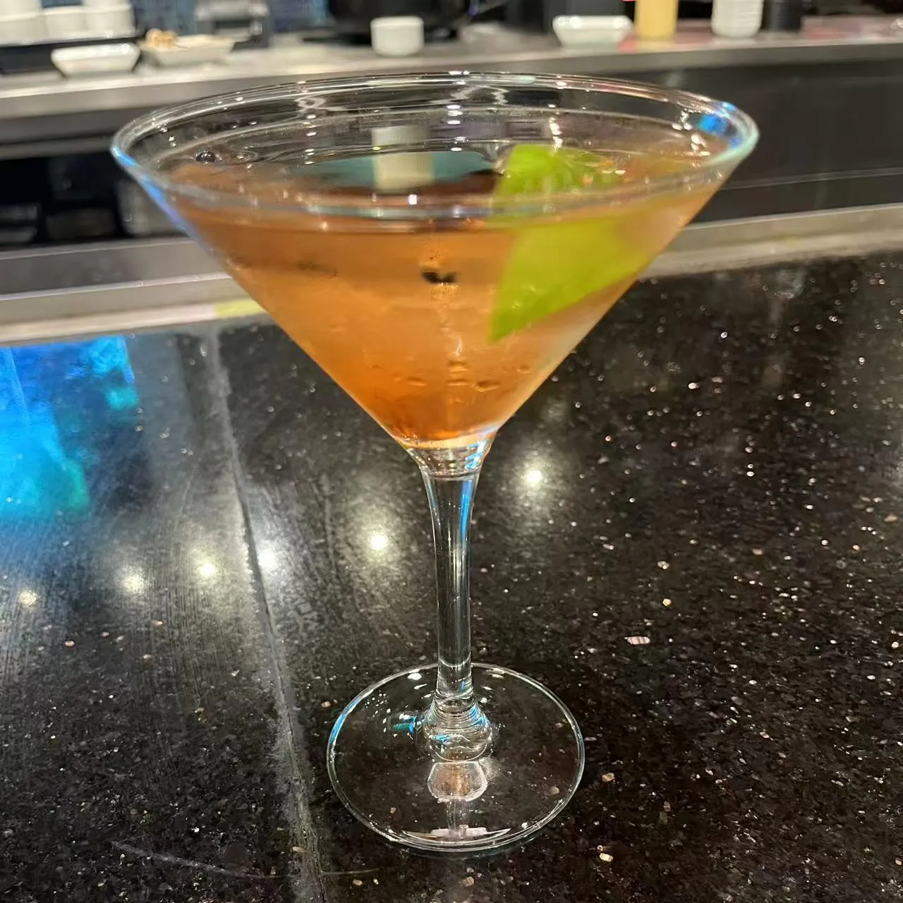 Amber martini cocktail garnished with fresh lime wedge on dark countertop